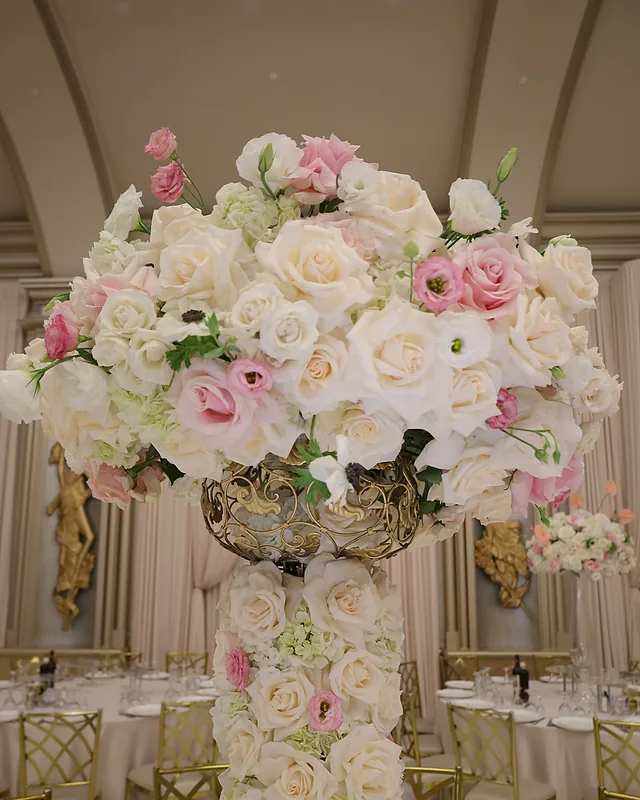 Tall pillar centerpiece of cream and blush roses, lisianthus and anemones in a ballroom