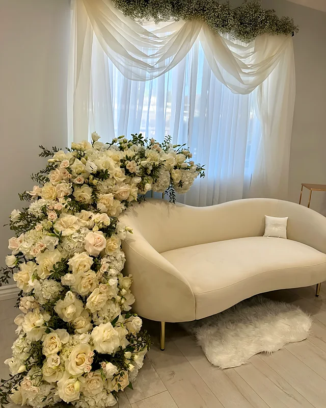 Cascading white rose and ranunculus installation beside a cream lounge sofa