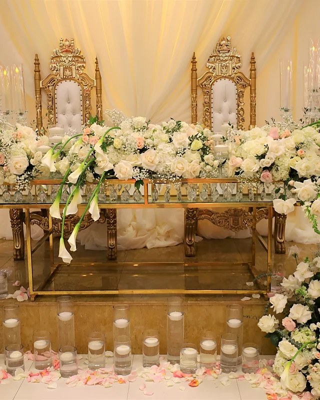Gold thrones behind a head table covered in white roses, calla lilies and baby's breath with floating candles