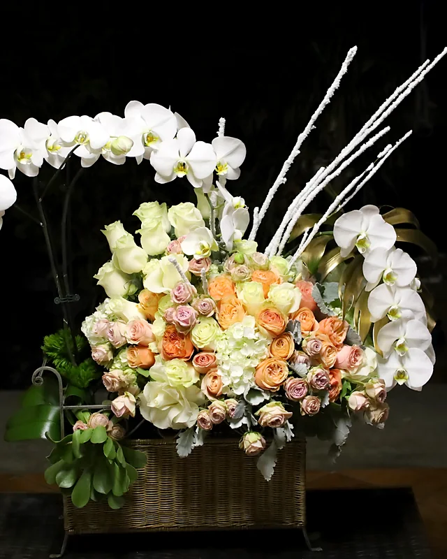 Grand arrangement of white orchids, peach garden roses and hydrangea in a woven basket