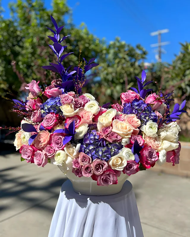 Purple hydrangea, rose and delphinium arrangement on a draped stand
