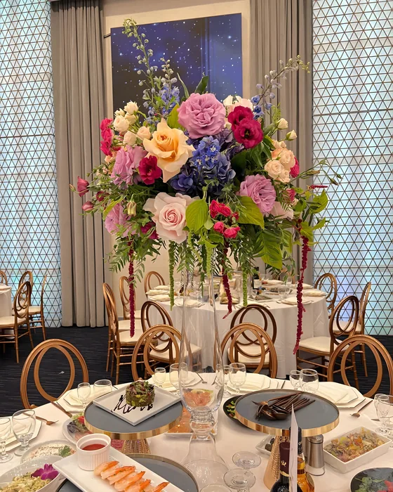 Tall colorful rose and delphinium centerpiece on a gold stand at a ballroom event