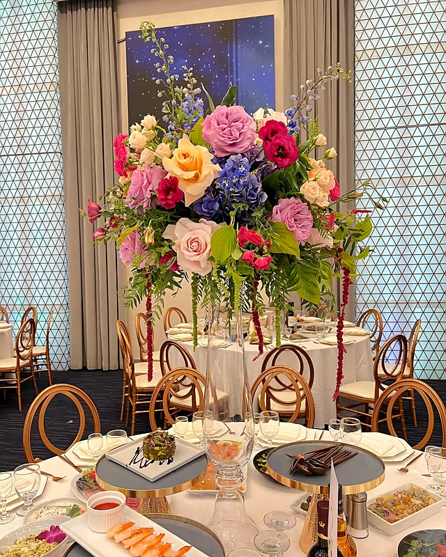 Tall colorful rose and delphinium centerpiece on a gold stand at a ballroom event