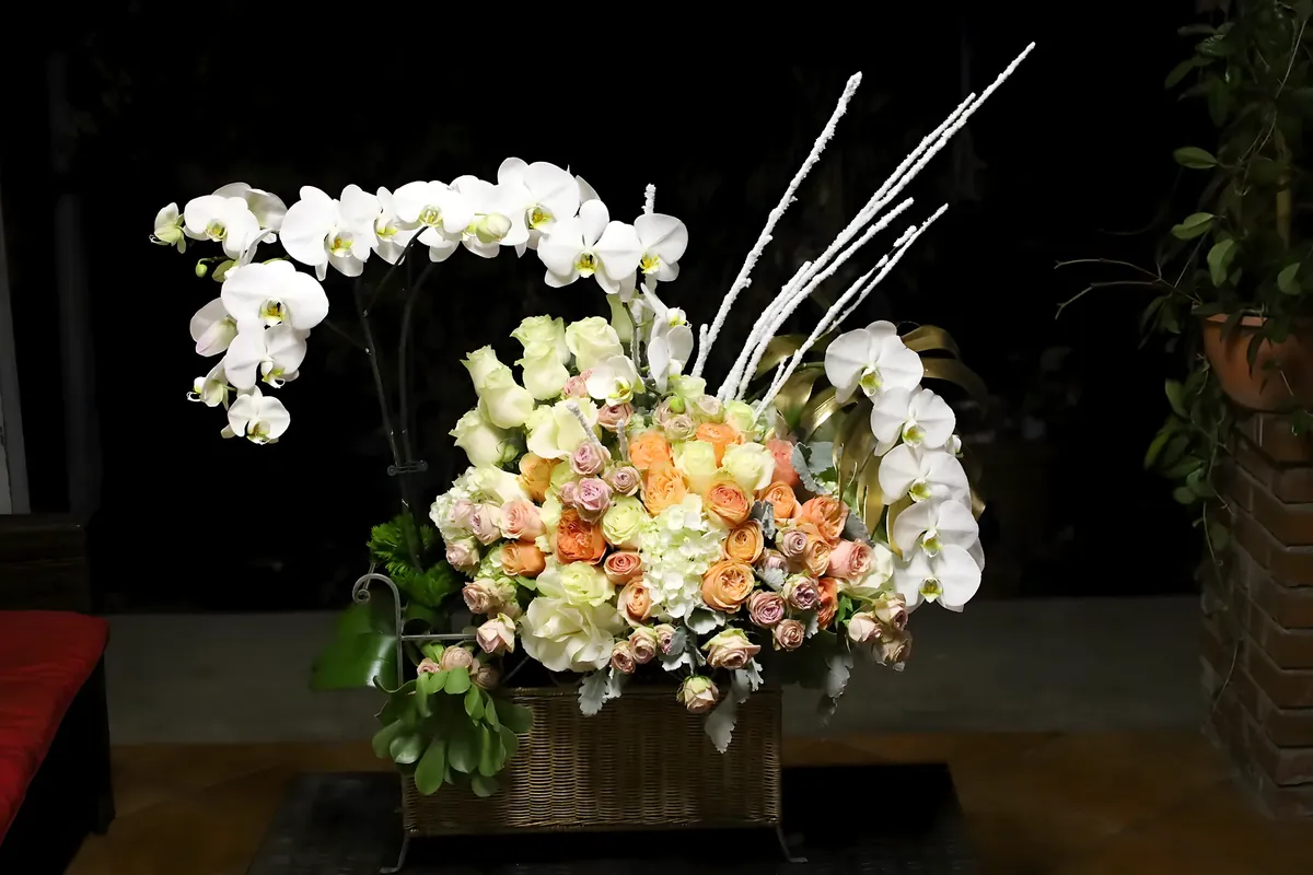 Grand arrangement of white orchids, peach garden roses and hydrangea in a woven basket