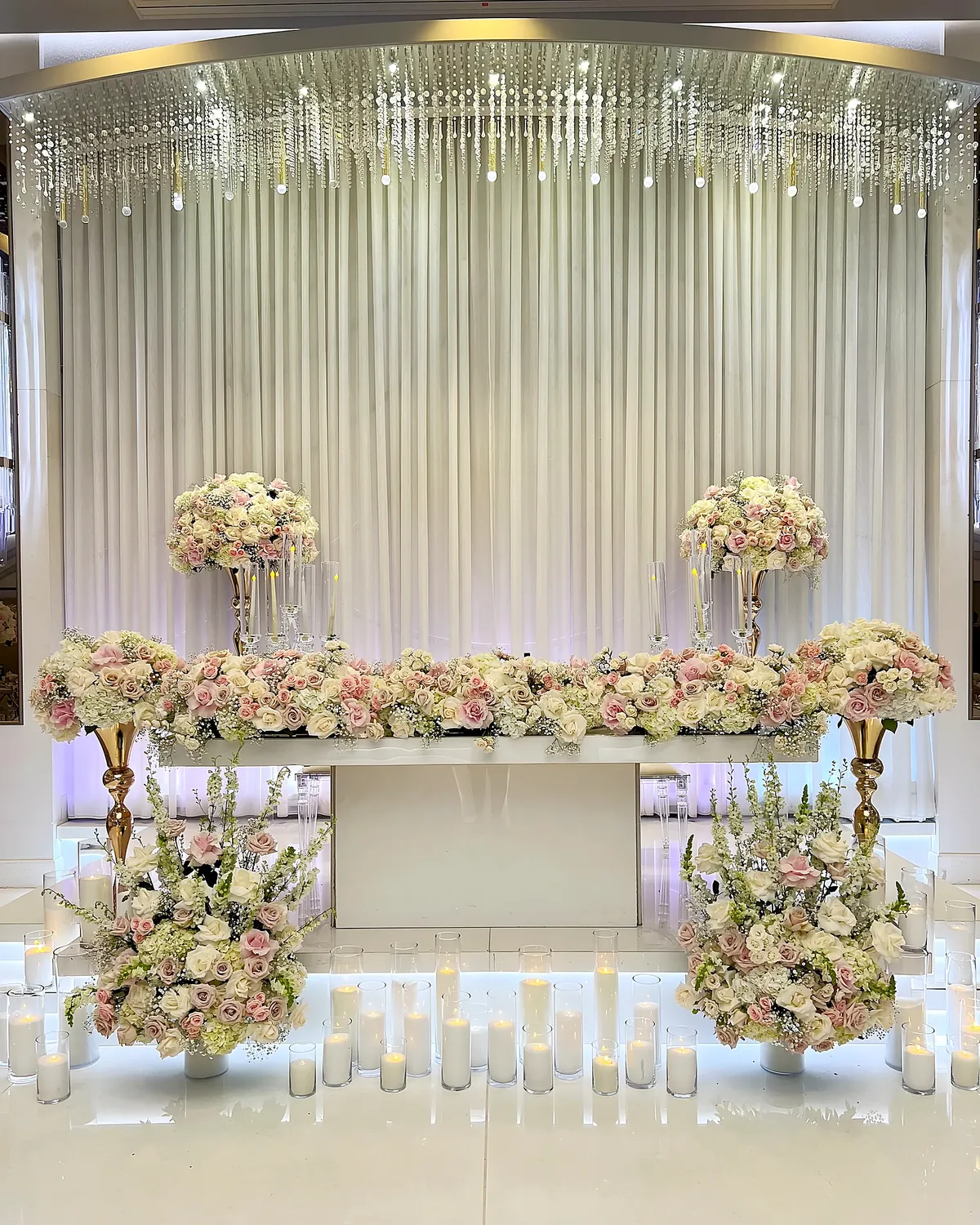 Wedding sweetheart table with blush floral garland, candles and a draped crystal backdrop